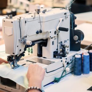 industrial overlock sewing machine and hands of seamstress at work in the garment factory